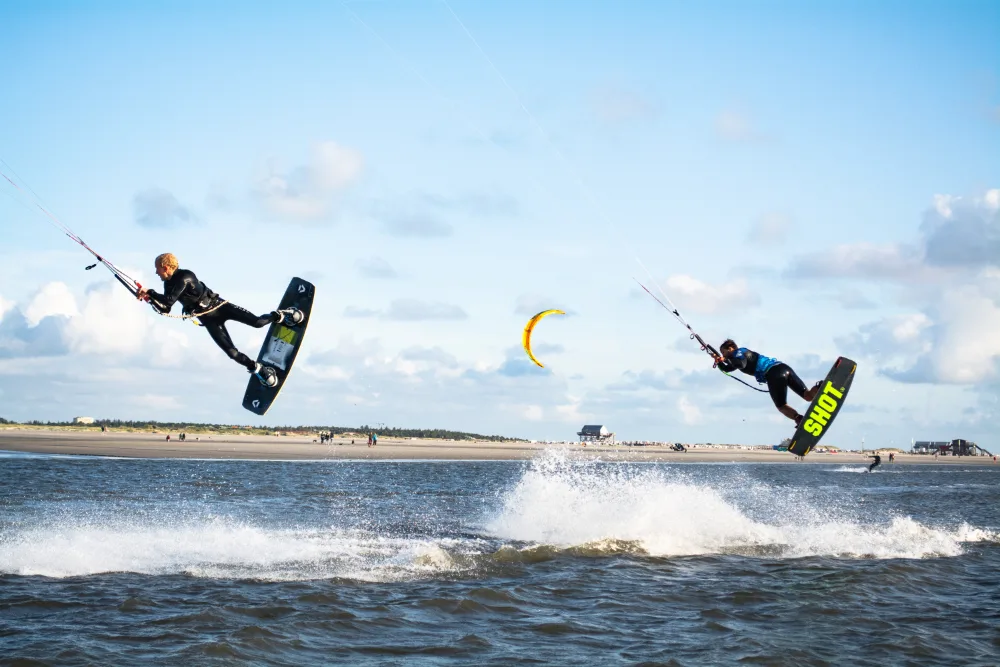 Zwei Kitesurfer bei Sprüngen über der Nordsee am Strand von St. Peter-Ording.